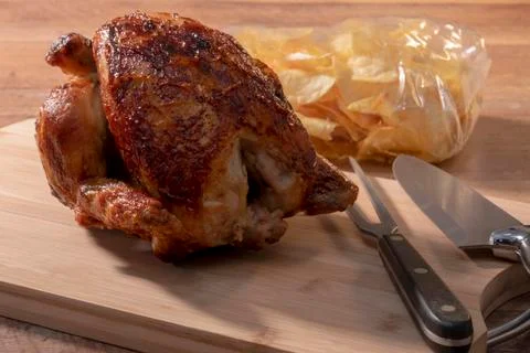 Select focus of a spit-roasted chicken on a wooden board with an out of focus Stock Photos