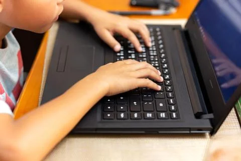 Selected focus childrens hand using laptop keyboard playing on dinner table. Stock Photos