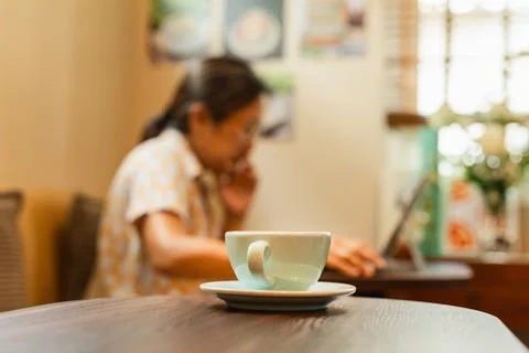Selected focus cup of coffee on table with woman working on laptop in blur Stock Photos