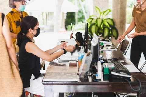 Selected focus receptionist with face shield giving envelope to guest in hotel. Stock Photos