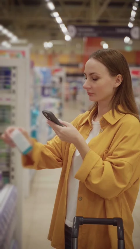 Selecting cosmetics in a store while checking details on a smartphone Stock Footage 305415919