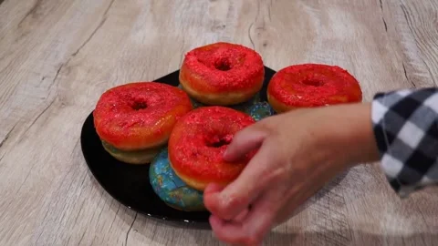 Selecting vibrant and eye-catching donuts from a beautifully arranged plate full Stock Footage 345884360