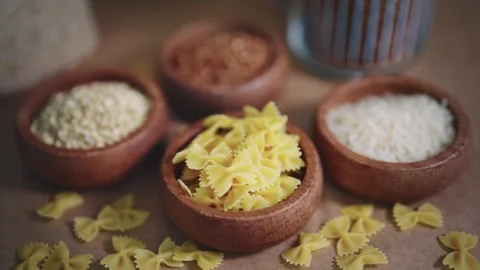 Selection of pasta, rice and grains in wooden bowls on rustic table. Natural Stock Footage 303639715