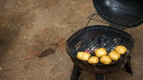 A selection of unwashed potatoes are placed on a charcoal grill, cooking with Stock Photos