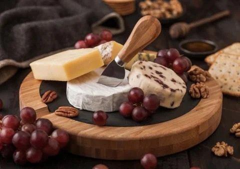 Selection of various cheese on the board and grapes on wooden table Stock Photos