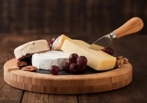 Selection of various cheese on the board and grapes on wooden table Stock Photos