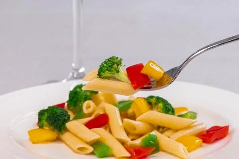 Selective focus and close up of a fork holding pasta and vegetables over an o Stock Photos