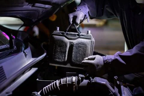 Selective focus to Auto mechanic wearing protective gloves replacing a 12V .. Stock Photos