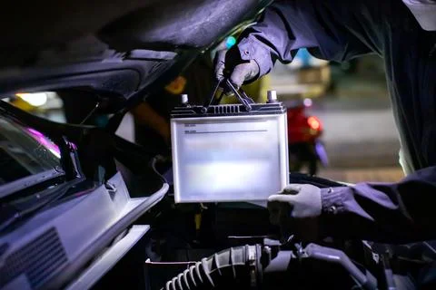 Selective focus to Auto mechanic wearing protective gloves replacing a 12V .. Stock Photos