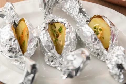 Selective focus of baked potatoes wrapped with tin foil on a plate. Tradition Stock Photos