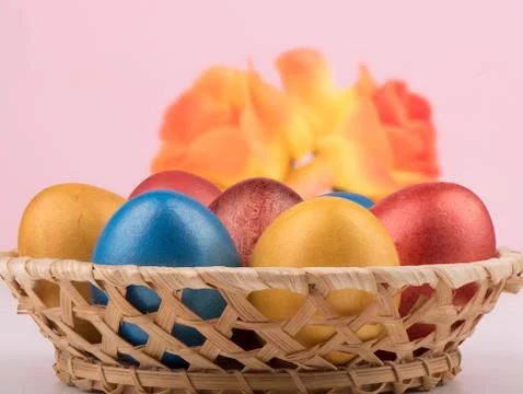 Selective focus. Basket with multi-colored Easter eggs and blurry flowers in the Stock Photos