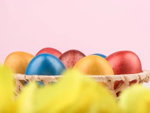 Selective focus. Basket with multi-colored Easter eggs and blurry yellow flowers Stock Photos