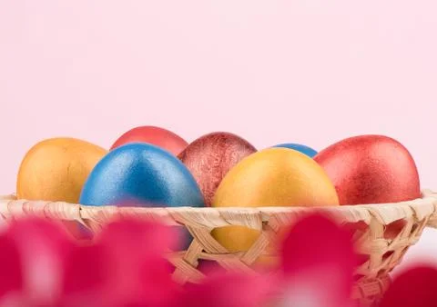 Selective focus. Basket with multi-colored Easter eggs and blurry red flowers in Stock Photos