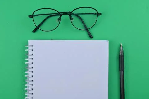 Selective focus of blank notebook , spectacles and pen on a green background. Stock Photos
