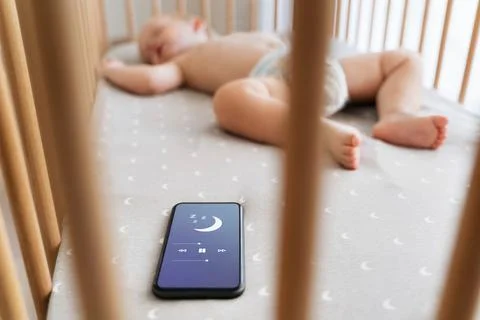 Selective focus of boy in crib falling asleep with the help of phone app for Stock Photos