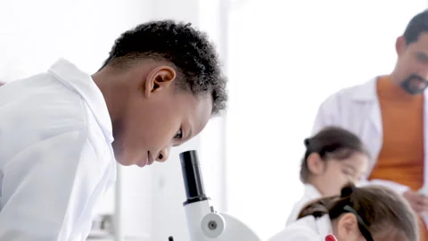 Selective focus of boy student in gown uniform research using microscope eq.. Stock Footage 243619057