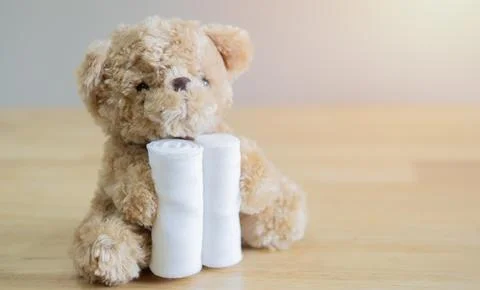 Selective focus of brown teddy bear holding a bandage on wooden table. Stock Photos