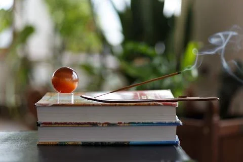 Selective focus, burning incense stick with brown glass ball on stack of books Stock Photos