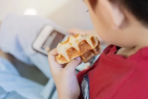 Selective focus of child sitting on sofa with waffle and smartphone in hands Stock Photos