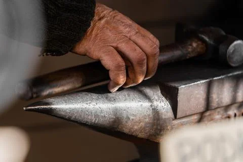 Selective focus close-up of a blacksmith's hand with a hammer metal anvil Stock Photos