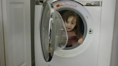 Selective focus close up of exploring playful girl hiding in washing machine 库存照片
