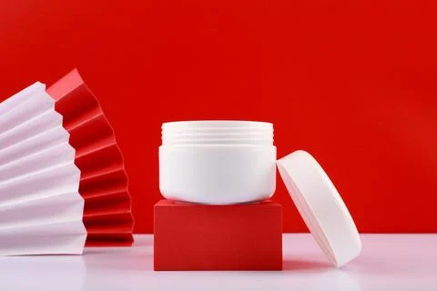 Selective focus, close up of white opened creme jar on red podium against red Stock Photos