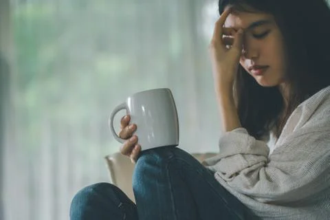 Selective focus coffee mug in hand of a sad woman sitting on a chair next to Stock Photos