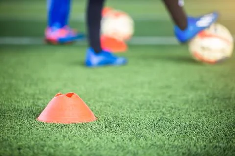 Selective focus to cone marker with blurry soccer team is on green artificial Stock Photos