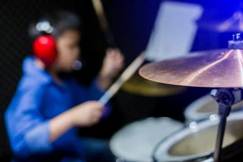Selective focus to cymbals of drum set with blurry kid put headphone to learn Stock Photos
