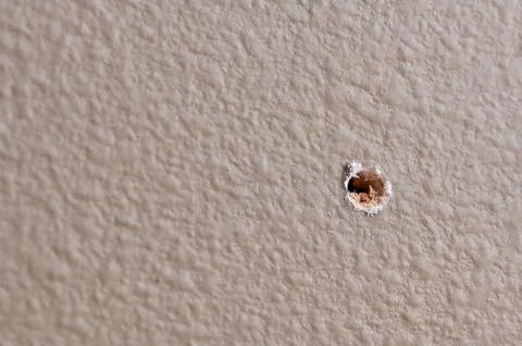 Selective focus on drilled hole through drywall with bits of insulation showing. Stock Photos