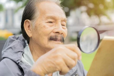 Selective focus of elderly man with magnifying glass in hand and reading a .. Stock Photos