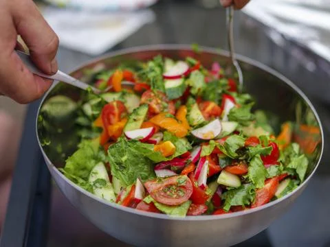 Selective focus of fresh chopped spring salad, man mixing salad, backyard Stock Photos