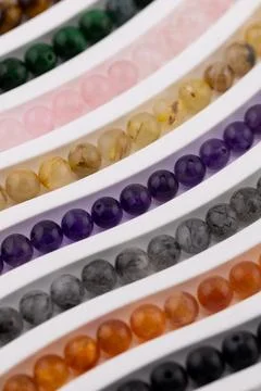 Selective focus gemstone bead strands in curved rows on white tray Stock Photos