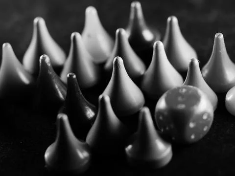 A selective focus grayscale shot of a die surrounded by triangular board game Stock Photos