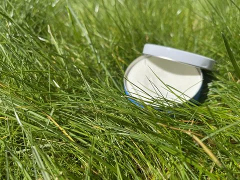 Selective focus on green grass, sunscreen cream on background, copy space Stock Photos