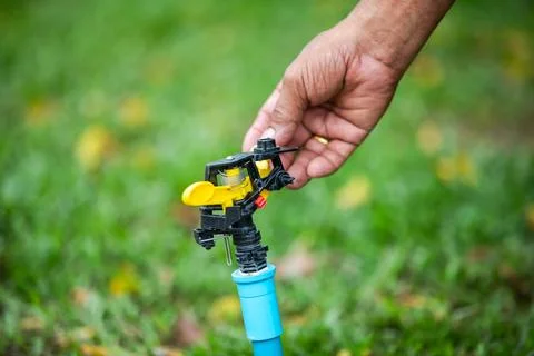 Selective focus to Hand adjusting yellow garden sprinkler nozzle on green l.. Stock Photos
