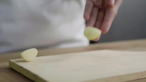 Selective focus of hand drops garlic onto a chopping board, preparing ingre.. Stock Footage 329703419