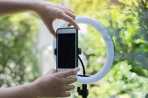 Selective focus of hands of influencer adjusting smart phone on ring light .. Stock Photos