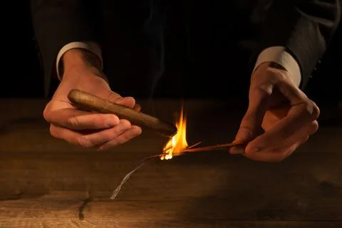 Selective focus on the hands of the man lighting up the cigar with help of .. Photos