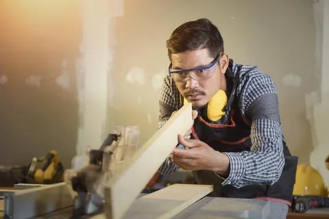 Selective focus of handsome man in goggles and apron in workshop,Carpenter wo Stock Photos