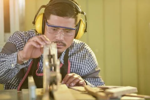 Selective focus of handsome man in goggles and apron in workshop,Carpenter wo Stock Photos