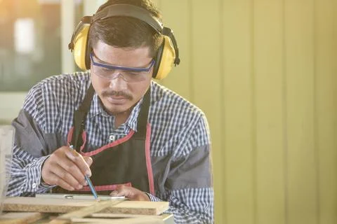 Selective focus of handsome man in goggles and apron in workshop,Carpenter wo Stock Photos