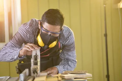 Selective focus of handsome man in goggles and apron in workshop,Carpenter wo Stock Photos