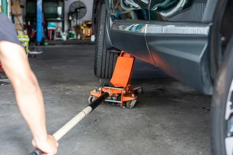 Selective focus to hydraulic floor jack with blurry hand of mechanic. Mecha.. Stock Photos