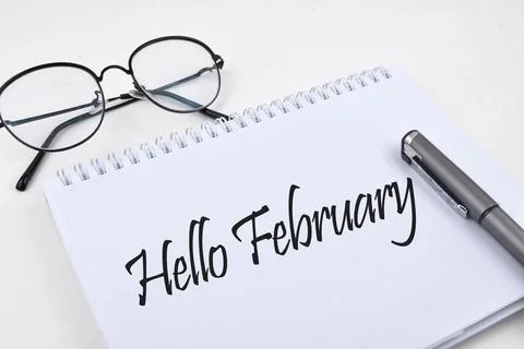 Selective focus image of pen and spectacles with Hello February wording. Busi Stock Photos