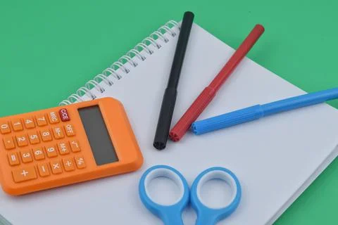 Selective focus image of pen,calculator and scissors with notebook on green b Stock Photos