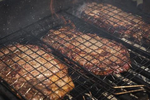 Selective focus of juicy beef steaks grilling on barbecue grid with smoke Stock Photos