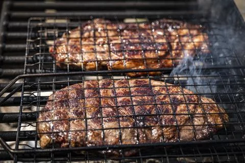 Selective focus of juicy beef steaks grilling on barbecue grid with smoke Stock Photos