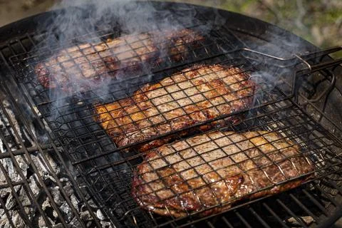 Selective focus of juicy beef steaks grilling on barbecue grid with smoke Stock Photos