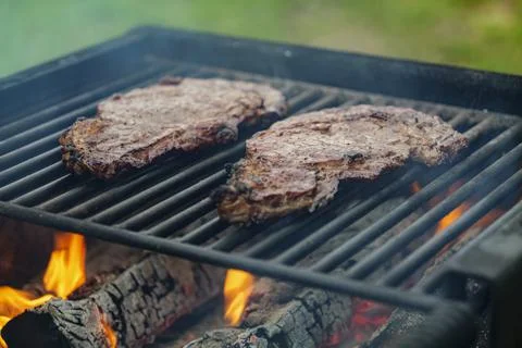 Selective focus of juicy beef steaks grilling on barbecue grid with smoke Stock Photos